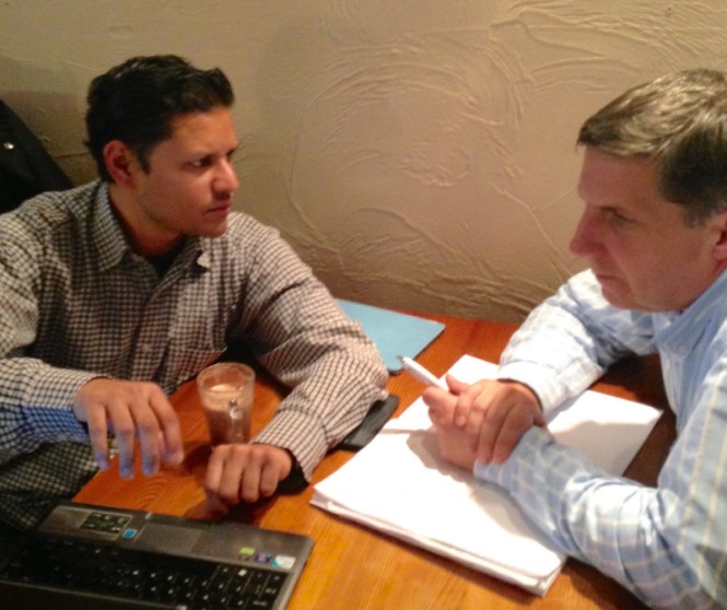 Photo of Deepak and John at a cafe table with a laptop