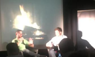 Photo of Joel Gascoigne and Nick Holzherr in front of screen with glowing fireplace